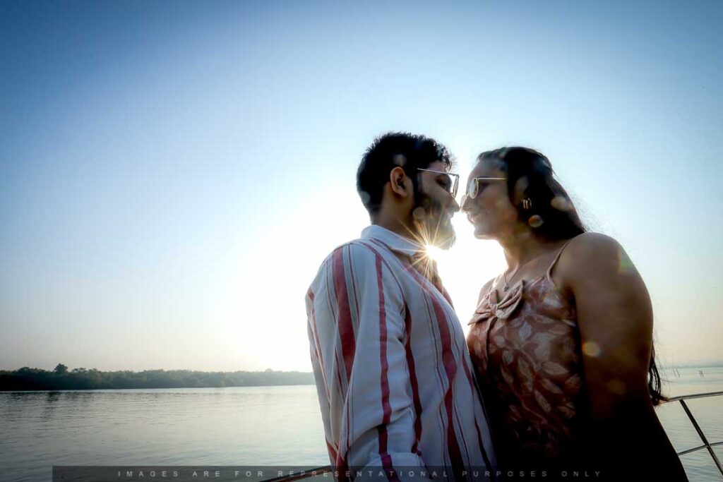 Romantic couple facing each other near a riverside at sunset during a pre-wedding photoshoot, with sunlight peeking through.