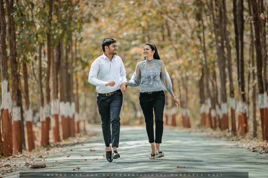 Happy couple holding hands and walking down a tree-lined path during a pre-wedding shoot.